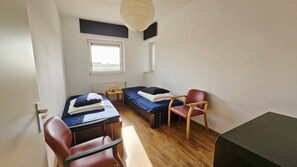 A small, well-lit room with two beds, a desk, a chair, and a window providing natural light. - Apartment with Sea Views in Breskens | Port Scaldis 19-031 (Breskens)
