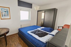A bedroom with a bed, a chair, a desk, a window, and a painting on the wall.