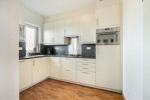 A kitchen with white cabinets, a black countertop, a stainless steel range hood, and a built-in oven.