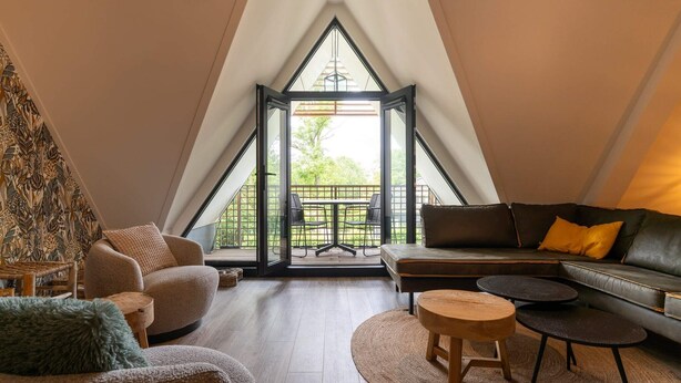 Acogedor dormitorio en áticos, de forma triangular, con un ventanal grande, un sofá, una mesita de centro y una mesa de comedor.
