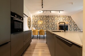 A modern kitchen with a built-in oven, a large island with a sink, and a dining area with two chairs.