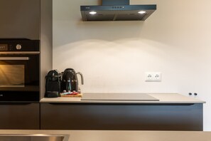 A modern kitchen with a built-in oven, a coffee maker, and a wall-mounted light. - Apartment with sauna near the sea in Oostkapelle | Duno Lodge (Oostkapelle)