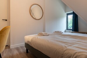 A bedroom with a bed, a round mirror, a chair, and a window with curtains. - Apartment with sauna near the sea in Oostkapelle | Duno Lodge (Oostkapelle)