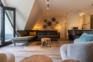 Un saló modern amb un sofà seccional, un tamboret de fusta petit i una zona de menjador amb taula i cadires.
