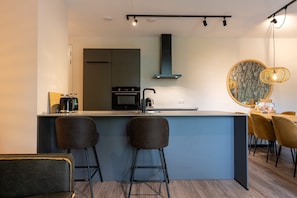 Une cuisine moderne dotée d’un îlot central, de tabourets de bar, d’un coin repas avec des chaises et d’un grand miroir.