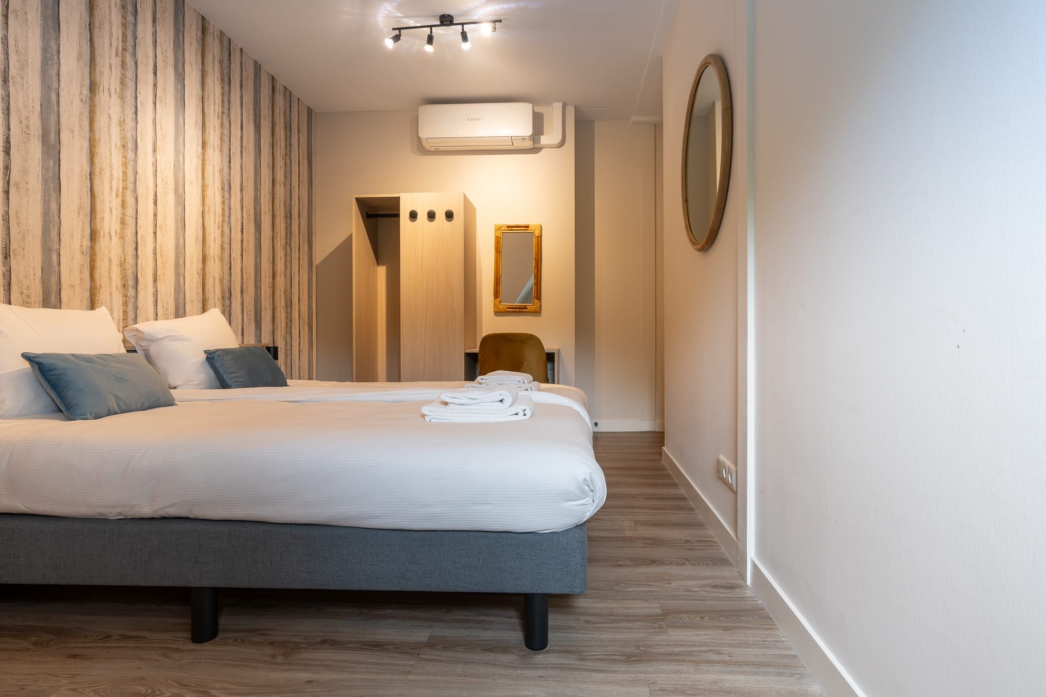A modern hotel room with a large bed, a wooden accent wall, a mirror, and a small seating area.