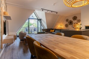Un espace repas moderne avec une grande table en bois, des sièges confortables et une vue dégagée sur l’extérieur grâce à une grande fenêtre.