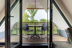 A modern balcony with a table and chairs, a wooden deck, and a view of greenery. - Apartment with sauna near the sea in Oostkapelle | Duno Lodge (Oostkapelle)