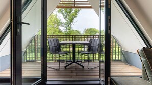 Un balcón con una mesa y sillas, vistas al exterior y una terraza de madera.