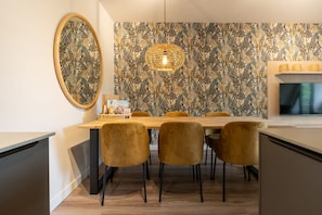 A dining area with a wooden table, four chairs, a wall-mounted TV, and a decorative light fixture. - Apartment with sauna near the sea in Oostkapelle | Duno Lodge (Oostkapelle)