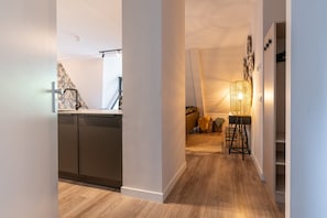 Une cuisine moderne dotée d’un lave-vaisselle encastré, d’un plancher en bois et donnant sur un espace de vie avec un canapé et une lampe.