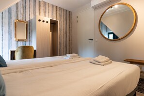 A hotel room with a large bed, a round mirror, a wardrobe, and a chair.