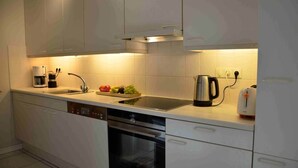 Ett modernt kök med vita skåp, diskmaskin, ugn, kaffebryggare, vattenkokare och brödrost.