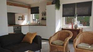 Een moderne keuken met witte kasten, een eetgedeelte met rieten stoelen en een bank.