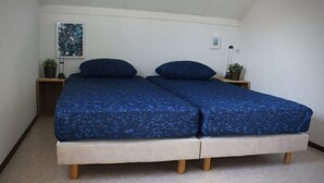 Een slaapkamer met twee eenpersoonsbedden, een klein nachtkastje met een lamp, en een lijst met een afbeelding aan de muur.