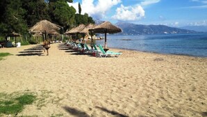 A beach with rows of sun loungers and thatched umbrellas, a clear sky, and a calm sea. - Beachfront villa 100 metres from the sandy beach (Kontokálion)