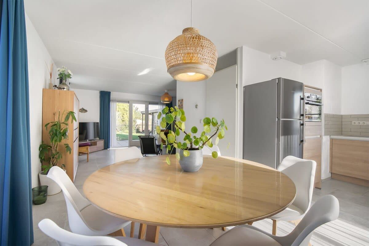 A modern dining area with a round wooden table, white chairs, and a hanging light fixture.