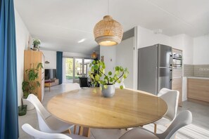 Uma sala de jantar moderna com uma mesa redonda de madeira, cadeiras brancas e um lustre.