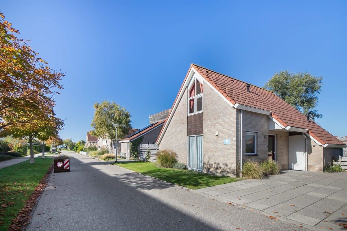 Eine Wohnstraße mit Häusern, blauem Himmel und einem Geschwindigkeitsbegrenzungsschild.