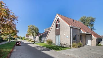 Eine Wohnstraße mit Häusern, blauem Himmel und einem Geschwindigkeitsbegrenzungsschild.