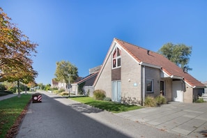 Una calle residencial con casas, cielo despejado y una señal de límite de velocidad.