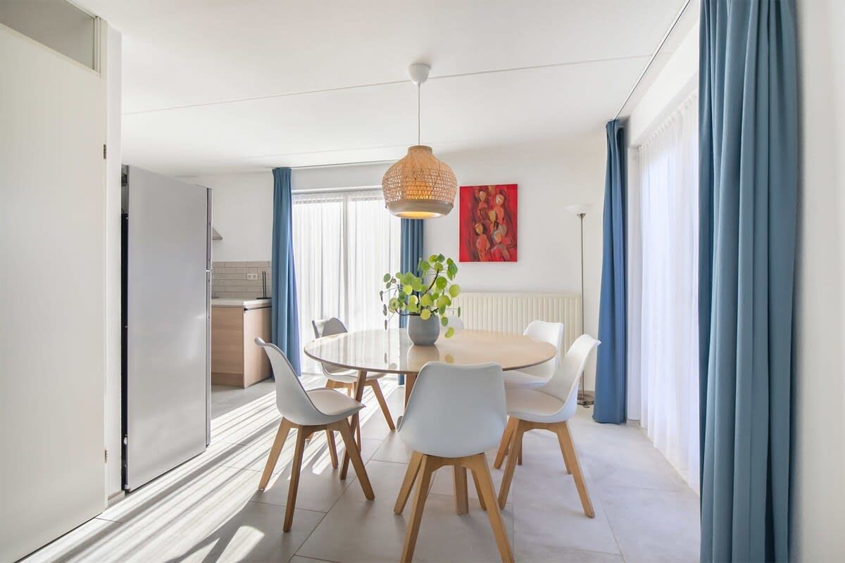 A modern dining area with a round table, white chairs, and a hanging light fixture.