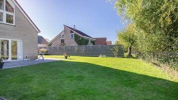 Ein Wohnhausgarten mit Rasen, Holzlattenzaun und einem Haus mit geneigtem Dach.