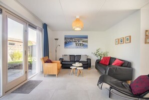 Una sala de estar moderna con sofá, sillón y una mesa de centro, una ventana grande con cortinas y un candelabro.