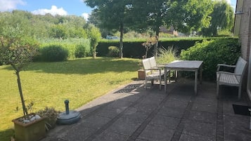 A patio with a table and two chairs, a small tree, and a well-maintained lawn.