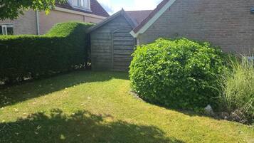 A well-maintained garden with a wooden shed, neatly trimmed hedges, and a grassy lawn.