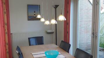 A dining area with a table, chairs, a blue bowl, hanging pendant lights, a painting, and a window with a view of a brick wall.