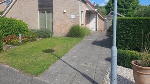 Ein zweistöckiges Wohngebäude mit Backsteinfassade, einer sichtbaren Tür und einem kleinen Garten mit einem Weg zum Eingang.