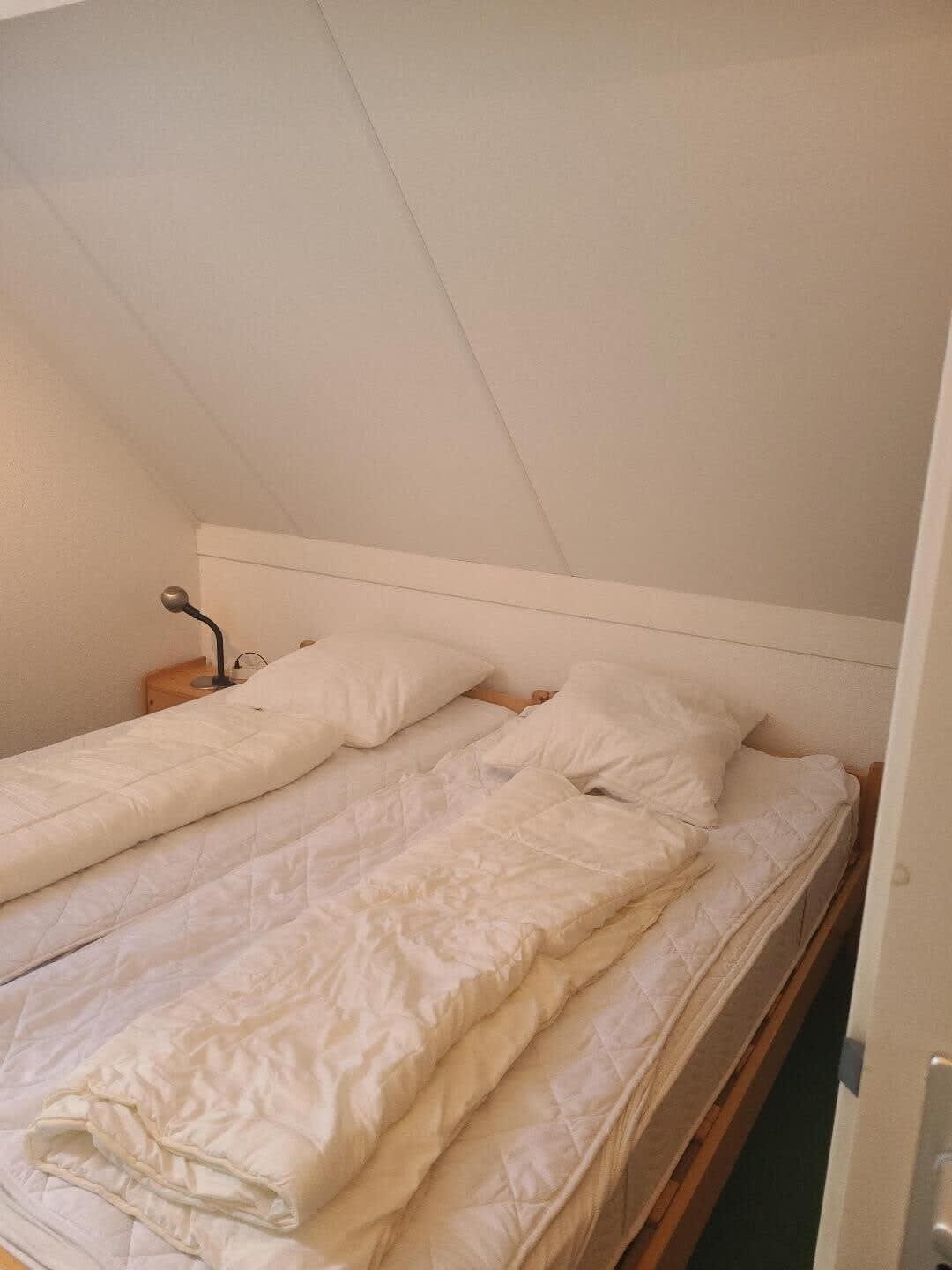 A single bed in a room with a sloped ceiling, a bedside table, and a lamp.