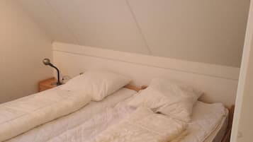 A single bed in a room with a sloped ceiling, a bedside table, and a lamp.