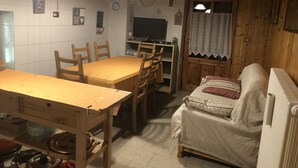 Une pièce chaleureuse avec une table à manger en bois, des chaises, un canapé, un téléviseur et une horloge au mur.