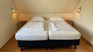 Une chambre double avec deux lits, chacun équipé d’un oreiller et d’une couverture, deux tables de chevet et un plafond en pente.