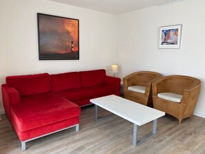 A red sofa, a white coffee table, and two wicker chairs in a room with a wooden floor and white walls.