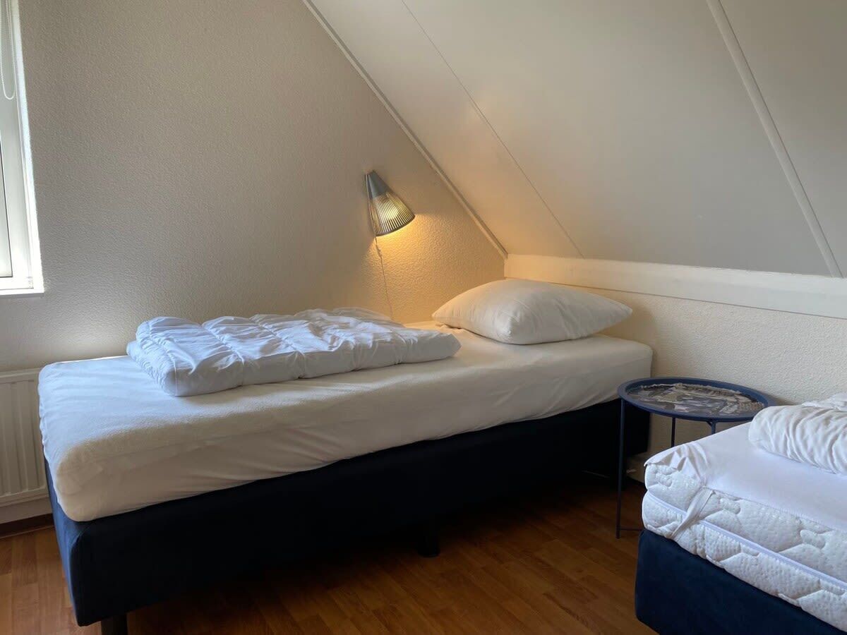 A small, neatly made room with a bed, a bedside table, and a lamp.