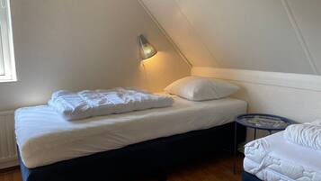 A small, neatly made room with a bed, a bedside table, and a lamp.