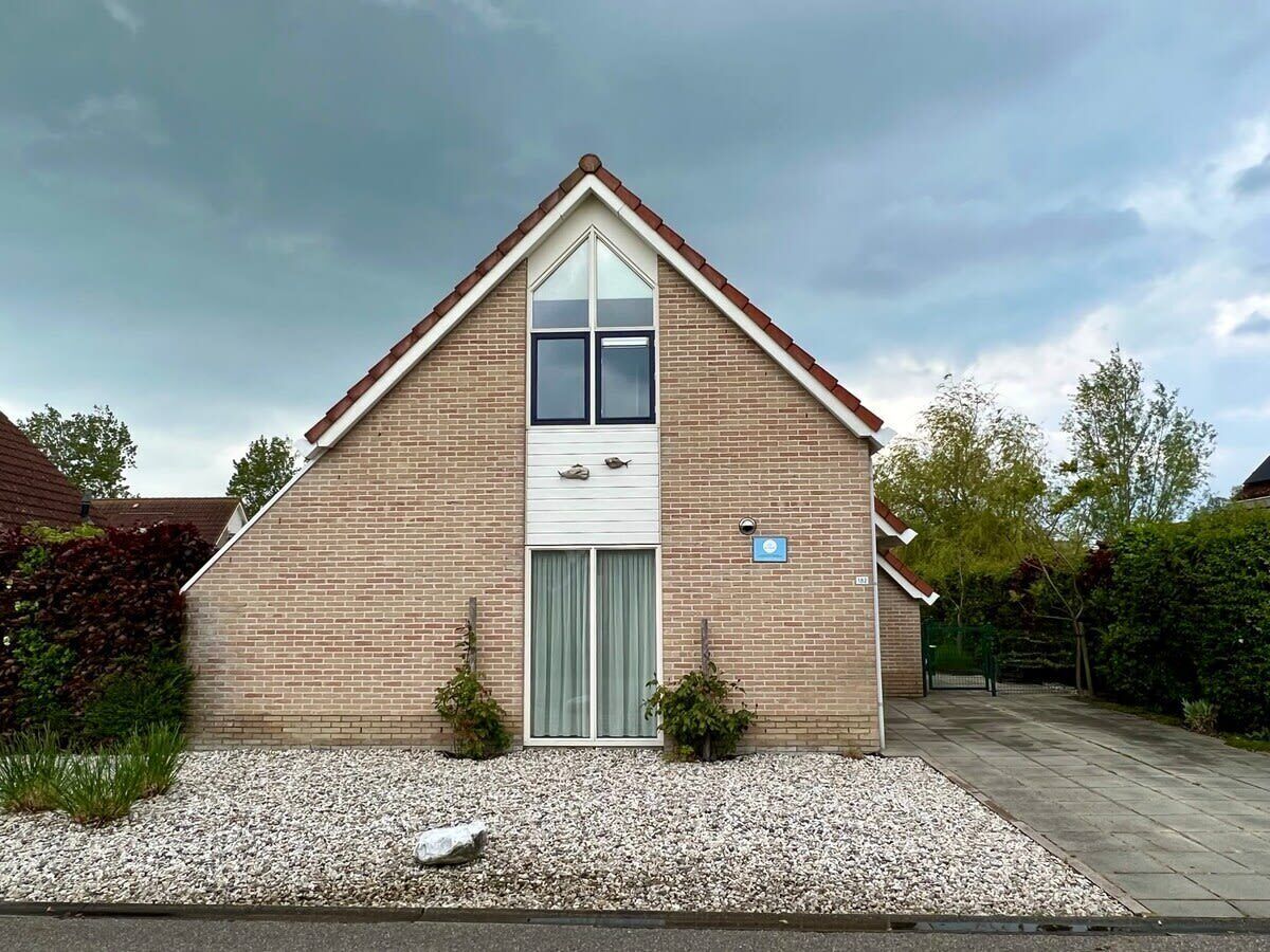 A single-story brick house with a pitched roof, a central entrance with a glass door, and a small garden area with gravel and plants.