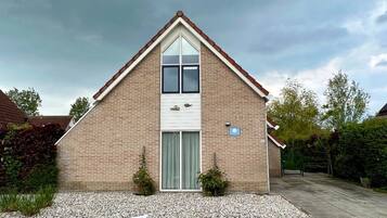 A single-story brick house with a pitched roof, a central entrance with a glass door, and a small garden area with gravel and plants.