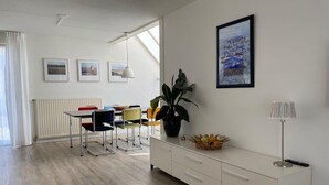 Un salon moderne avec un coin repas, des meubles blancs, une plante en pot et des œuvres d’art accrochées au mur.