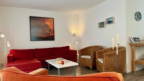 Un salon avec un canapé rouge, une table basse blanche, une chaise en bois, une lampe et un tableau accroché au mur.