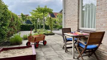 A patio with a table and chairs, a wooden cart, and a brick wall.