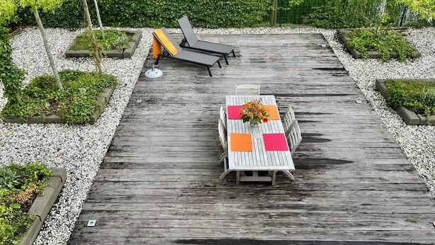 Une terrasse en bois avec une table et des chaises, entourée de gravier et de verdure.