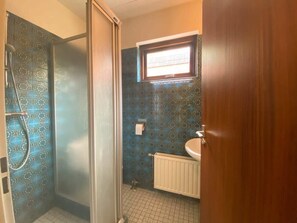 A bathroom with a shower, a toilet paper holder, and a window.