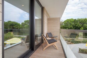 A balcony with two wooden lounge chairs, a glass railing, and a view of greenery. - Studio with AC in Domburg | Summum Suites 4 (Domburg)