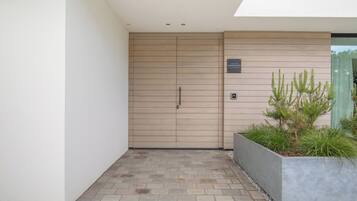 Entrada de un edificio moderno con puerta de madera, un letrero encima y una jardinera con plantas.