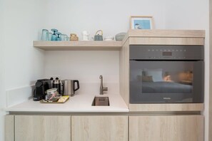 Une petite cuisine équipée d’un four encastré, d’une machine à café et d’un évier.