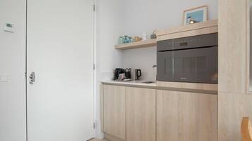 Eine kompakte Küche mit Einbauofen, Kaffeemaschine und einem Regal mit Gläsern.